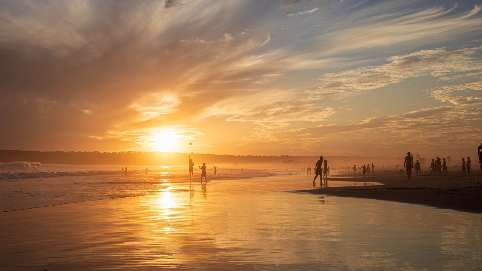 Golden sunset over the beach with people walking along the shore